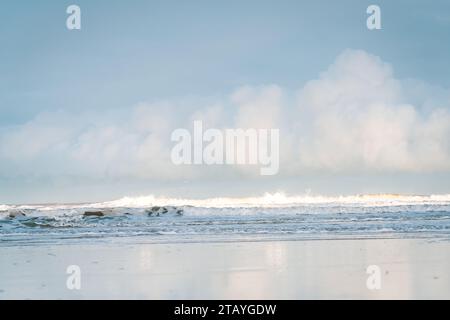 Beobachten Sie die weißen Wellen am Longsands Beach Tynemouth mit Surfern, die an einem eisigen Wintertag mit Schnee am Strand und hellblauem Himmel Wellen fangen. Stockfoto