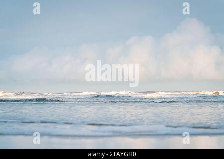 Beobachten Sie die weißen Wellen am Longsands Beach Tynemouth mit Surfern, die an einem eisigen Wintertag mit Schnee am Strand und hellblauem Himmel Wellen fangen. Stockfoto