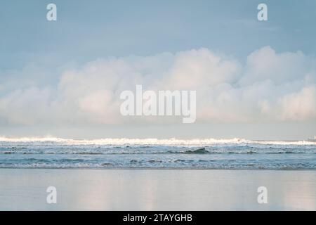 Beobachten Sie die weißen Wellen am Longsands Beach Tynemouth mit Surfern, die an einem eisigen Wintertag mit Schnee am Strand und hellblauem Himmel Wellen fangen. Stockfoto