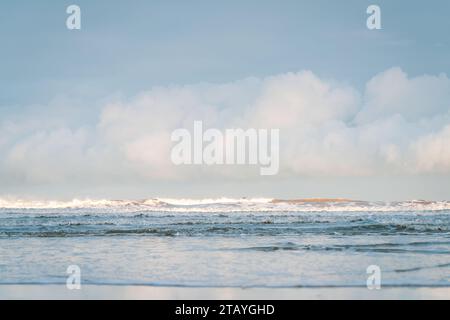 Beobachten Sie die weißen Wellen am Longsands Beach Tynemouth mit Surfern, die an einem eisigen Wintertag mit Schnee am Strand und hellblauem Himmel Wellen fangen. Stockfoto