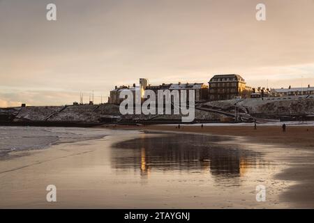 Reflexion des Grand Hotels in Tynemouth über den nassen Sand von Longsands Beach bei Sonnenuntergang im Dezember mit Schnee am Strand Stockfoto