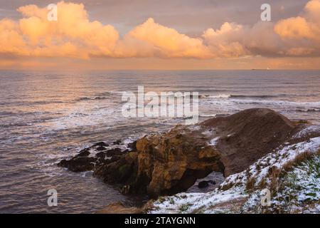 Sonnenuntergang mit orangefarbenem Himmel mit Cullercoats Watch House vorne, bedeckt mit Schnee und Gerüsten, die für sein Restaurierungsprojekt benötigt werden Stockfoto