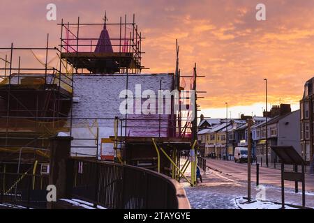 Sonnenuntergang mit orangefarbenem Himmel mit Cullercoats Watch House vorne, bedeckt mit Schnee und Gerüsten, die für sein Restaurierungsprojekt benötigt werden Stockfoto