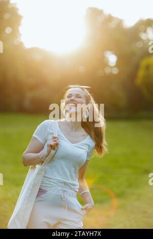 Sommerzeit. Glückliche stilvolle 40-jährige Frau in weißem Hemd mit Tragetasche auf der Wiese draußen in der Natur. Stockfoto