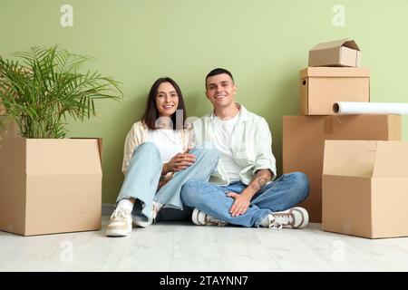 Glückliches junges Paar mit Umzugskartons, das neben der grünen Wand sitzt Stockfoto