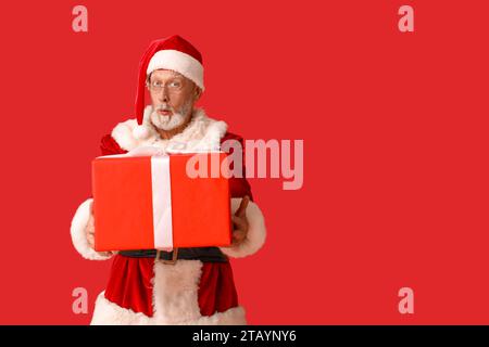 Schockierter Weihnachtsmann in Gläsern mit Geschenkbox auf rotem Hintergrund Stockfoto