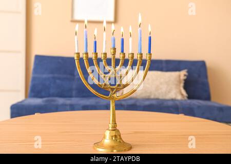 Menora mit brennenden Kerzen auf hölzernem Couchtisch im Wohnzimmer, Nahaufnahme. Hanukkah-Feier Stockfoto