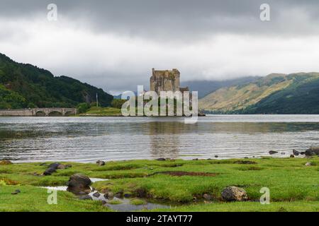 Blick von einer grasbewachsenen Küste auf das Eilean Donan Castle und die Brücke in Schottland Stockfoto