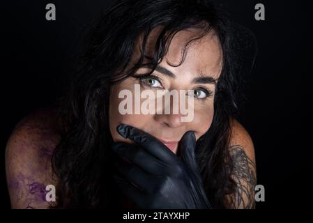 Nahaufnahme eines wunderschönen Tätowierers, der schwarze Handschuhe vor schwarzem Hintergrund trägt Stockfoto