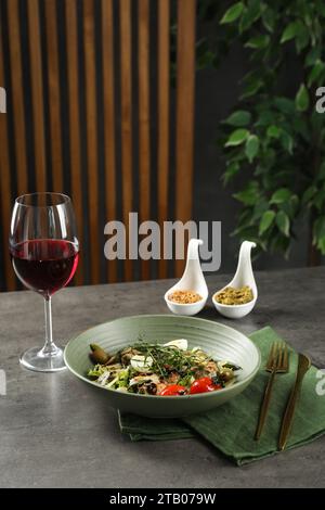 Leckeres Gericht mit Estragon, Salatdressings und einem Glas Wein auf grauem Tisch Stockfoto