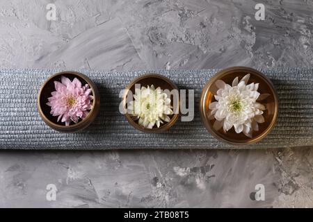 Tibetische Klangschalen mit Wasser, wunderschöne Chrysanthemen-Blumen auf grauem, strukturiertem Tisch, Blick von oben Stockfoto