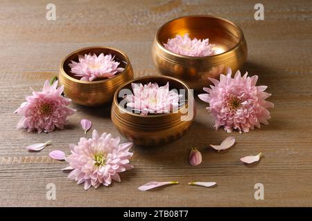 Tibetische Klangschalen mit Wasser und wunderschönen Blumen auf Holztisch Stockfoto