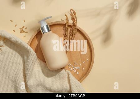 Reis und eine Flasche Duschgel ohne Marke sind auf einem runden Holztablett ausgestellt. Beigefarbener Hintergrund mit Blattschatten. Exquisiter Raum für kosmetische Werbung Stockfoto