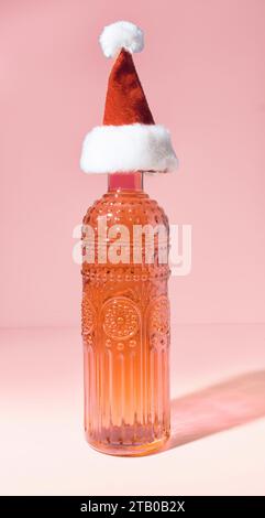 Eine Vintage Orange Champagnerflasche aus weißem Glas mit Weihnachtsmann-Hut auf orangefarbenem Hintergrund Stockfoto