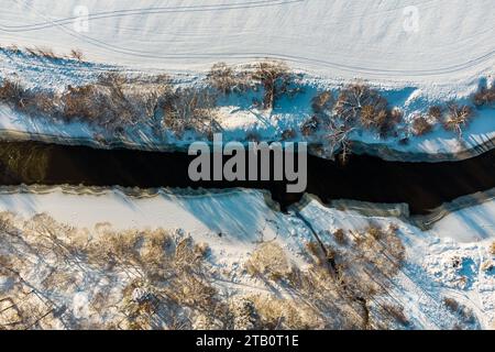 Blick von einer Drohne auf ein Flussbett, das im Winter in schneebedeckter Natur ungefroren ist Stockfoto