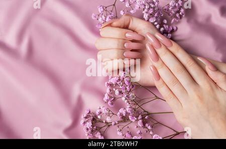 Weibliche Hände mit schöner Maniküre mit Gipsofila-Blüten auf rosa Seide Stockfoto