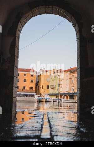 Überschwemmendes Meerwasser im Hafen von Cres Stadt, Blick durch einen Steinbogen eines Hauses. Schöne Aussicht durch das Tor, das Meer ist etwas überflutet. Stockfoto