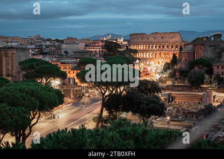 Abendlicher Blick auf das berühmte rom kolosseum, von weitem gesehen. Sichtbare Straße und Bäume, die zum berühmten Amphitheater führen, andere Häuser und Ruinen sichtbar sind Stockfoto