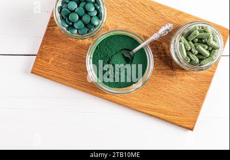 Grünes Spirulina-Pulver, runde Tabletten, Kapseln in verschiedenen Glasschüsseln und Gläsern auf einem Holzständer. Draufsicht. Ein super Nahrungsergänzungsmittel Stockfoto