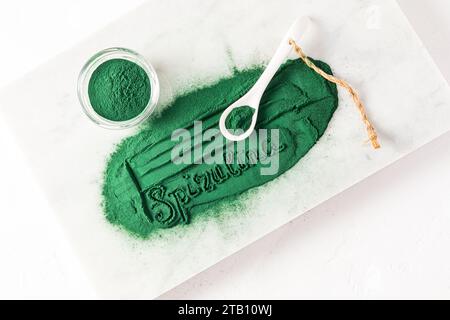 Eine wunderschöne Inschrift aus grünem Spirulina-Pulver und einem Keramiklöffel, der damit gefüllt ist. Weißer Hintergrund. Natürliche Nahrungsergänzungsmittel Stockfoto