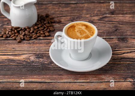 Espresso Macchiato in weißer Porzellanschale mit Milch und Kaffeebohnen auf Holztisch Stockfoto