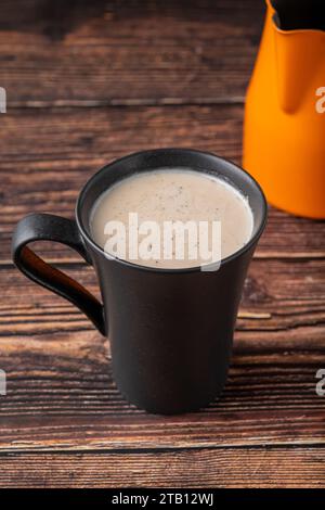 Milch mit türkischem Kaffee in schwarzer Tasse auf Holztisch Stockfoto