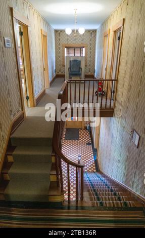 Eine Holztreppe mit einem geschwungenen Geländer und gestreiftem Läufer führt in einen Flur im Obergeschoss, William Howard Taft National Historic Site, Ohio. Stockfoto