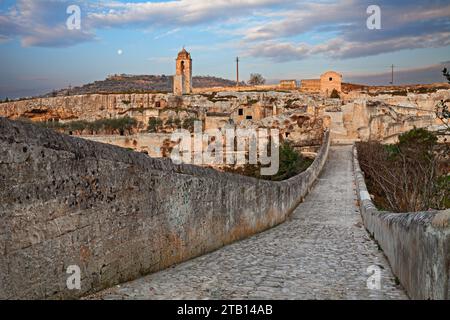 Gravina in Apulien, Bari, Italien: Landschaft bei Sonnenaufgang von der alten Aquäduktbrücke der alten Felsenkirche und den Höhlenhäusern, die in den Tuff gehauen wurden Stockfoto