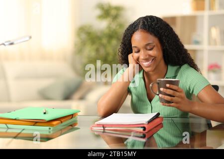 Schwarzer glücklicher Student trinkt Kaffee und lernt zu Hause Notizen lesen Stockfoto