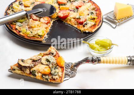 Pizzascheibe auf Schaufel. Fertige Pizza auf schwarzem Teller. Pizzaschneider. Weißer Hintergrund. Draufsicht Stockfoto