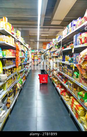 22. November, Surabaya. Indonesien. Eine muslimische Frau im Hijab schiebt einen Einkaufswagen an ermäßigten Lebensmitteln in einem hell beleuchteten Supermarktgang vorbei. E Stockfoto