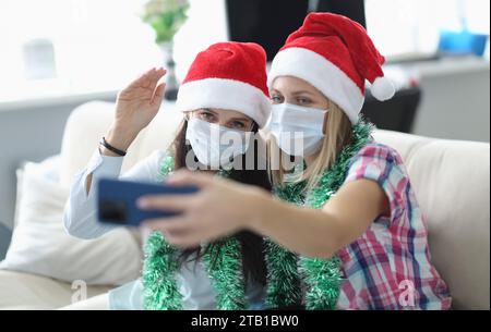 Zwei Frauen in Schutzmaske und weihnachtsmann Hut sprechen online am Telefon. Stockfoto