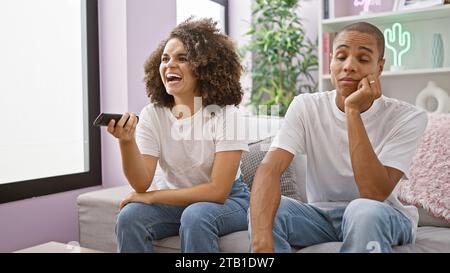 Ein wunderschönes Paar sieht sich fröhlich ihren Lieblingsfilm an, sitzt zu Hause auf der Couch, teilt ein Lächeln und lacht Stockfoto