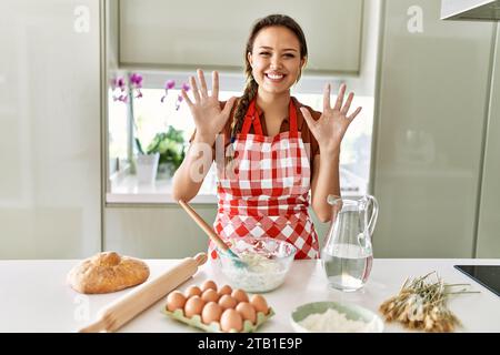 Junge, wunderschöne hispanische Frau, die selbstbewusst lächelt und in der Küche Hände mit Mehl zeigt Stockfoto
