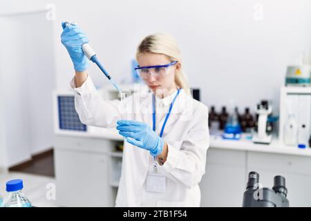 Junge blonde Wissenschaftlerin, die im Labor Flüssigkeit auf das Reagenzglas gießt Stockfoto