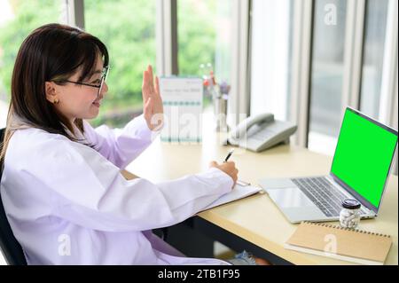 Asiatischer Arzt im weißen Mantel benutzte Laptop, der Videoanrufe mit grünem Bildschirm machte Stockfoto