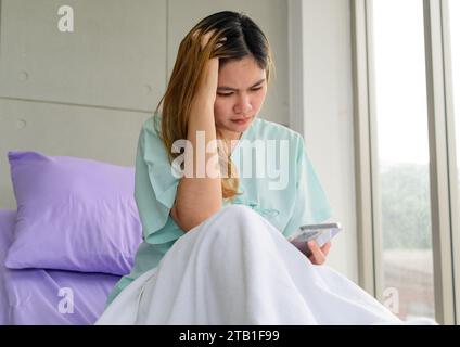 Gestresste Patientin, die Smartphone auf dem Krankenhausbett sieht Stockfoto