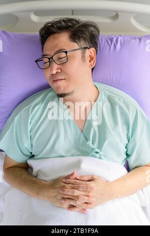 Asiatischer Mann, der im Bett liegt und auf der Krankenhausstation schläft Stockfoto