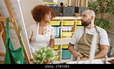 Im Atelier sitzen zwei lächelnde Künstler, Partner der Kreativität, zusammen, beschäftigen sich mit der Malerei von Leinwand und schwelgen in der Freude der Kunst von hinten Stockfoto