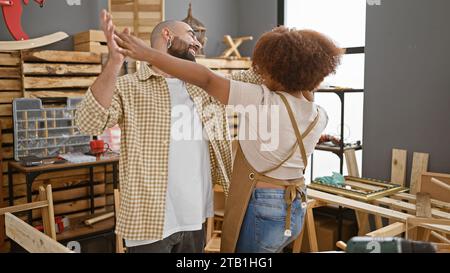 Lächelnde Zimmerleute, Mann und Frau, tanzt selbstbewusst zur Musik im Herzen ihrer Tischlerei, um ihren Beruf und den Rhythmus von zu genießen Stockfoto