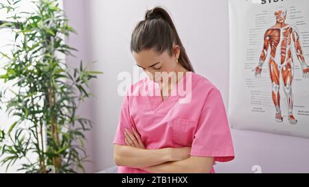 Traurigkeit durchdringt die Reha-Klinik, während die junge, schöne hispanische Therapeutin Müdigkeit und gekreuzte Arme in Innenräumen zeigt Stockfoto