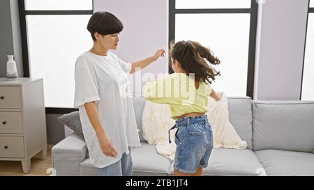 Fröhliche Mutter und Tochter tanzen selbstbewusst zusammen, strahlen Glück im Wohnzimmer ihres Hauses aus, während sie ein fröhliches Lied hören. Stockfoto