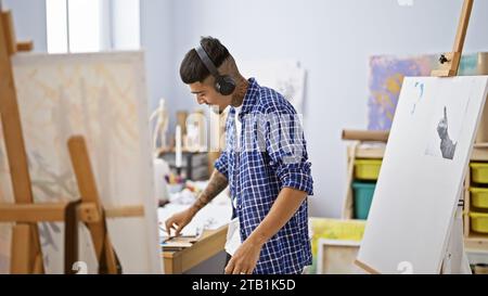 Porträt eines tätowierten jungen lateinmannes, ein Künstler, der in seine Zeichnung vertieft ist und in seinem Kunststudio inspirierende Audiosignale über Kopfhörer hört Stockfoto