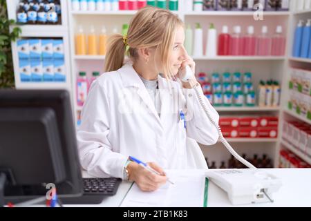 Junge kaukasische Frau, die in einer Apotheke arbeitet, spricht am Telefon und blickt zur Seite, entspannt Profilpositionen mit natürlichem Gesicht und selbstbewusster smil Stockfoto