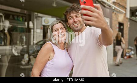 Fröhliche Mutter und Sohn fangen ihre glücklichen Momente zusammen ein und machen mit ihrem Smartphone ein cooles Selfie auf der Straße der Stadt Stockfoto