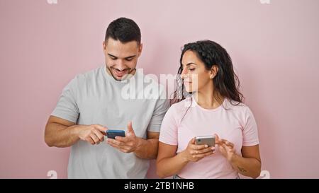 Mann und Frau, die Smartphones benutzen und über einen isolierten pinken Hintergrund lächeln Stockfoto