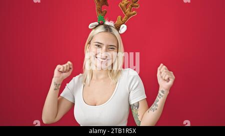 Junge schöne hispanische Frau mit Rentier-weihnachtshut, die über isoliertem roten Hintergrund tanzt Stockfoto