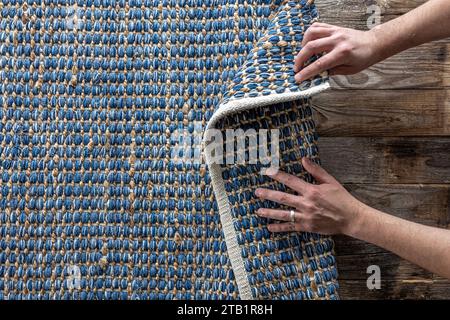 Mann, der Hand gewebte geometrische Denim-Teppich auf einem Holzboden zu Hause rollte. Stockfoto