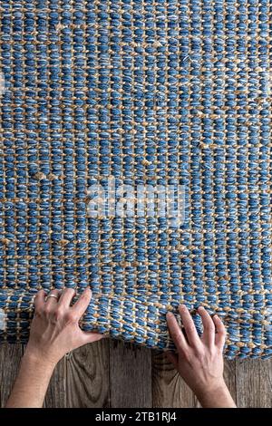 Mann, der Hand gewebte geometrische Denim-Teppich auf einem Holzboden zu Hause rollte. Stockfoto
