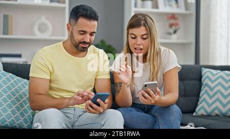 Mann und Frau, die zu Hause auf dem Sofa sitzen und Smartphones benutzen Stockfoto